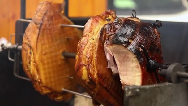 Grandes pedaços de deliciosos presuntos de porco cozidos em uma fogueira. A comida de rua. Comida ao ar livre. Acampar e cozinhar em um cuspo sobre o fogo, o homem cozinha grandes pedaços de carne em um cuspo no fogo, close-up — Vídeo de Stock