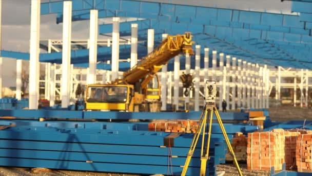 Teodolito óptico, Constructores Teodolito, teodolito de construcción en el fondo de la construcción de un gran edificio industrial o almacén, trabajos de construcción — Vídeo de stock