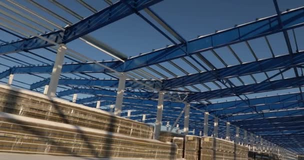 Moderna construcción de almacén, la estructura estructural de acero de un nuevo edificio comercial contra un cielo azul claro en el fondo, la construcción de una fábrica o almacén moderno — Vídeo de stock