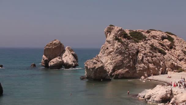 La gente si bagna e prende il sole su una piccola spiaggia di sabbia, il luogo di nascita di Afrodite sull'isola di Cipro, Rocce sporgono dall'acqua del mare, Bella spiaggia nel Mar Mediterraneo, spiaggia rocciosa — Video Stock