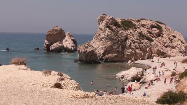 Pessoas tomar banho e tomar sol em uma pequena praia de areia, o local de nascimento de Afrodite na ilha de Chipre, Pedras ficar fora da água do mar, Praia bonita no Mar Mediterrâneo, praia rochosa — Vídeo de Stock