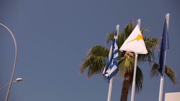 Banderas de la Unión Europea, Grecia, Chipre, la ciudad de Aya Napa, Grecia, Banderas en el asta de la bandera, el viento ondeando la bandera, Banderas en el asta de la bandera, la bandera ondeando viento, contra el fondo del cielo azul — Vídeos de Stock