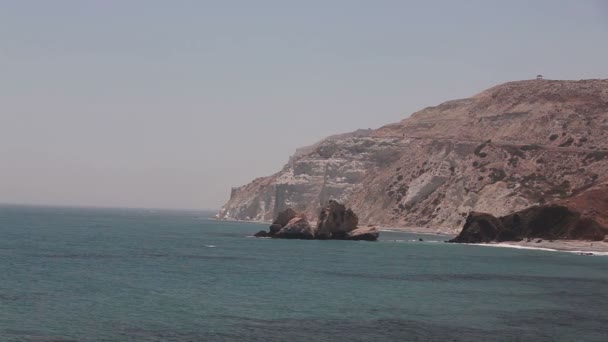 Der Berg, der ins Meer hinausgeht, die Meeresküste mit Felsen, blauem Himmel, Sandstrand, Meereswellen, Griechenland, Zypern, Aphrodite-Pool, wunderschöne majestätische Landschaft, felsiger Strand hohe Klippen blauer Himmel und Meer — Stockvideo