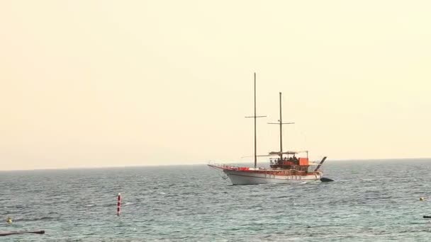 Nave a vela galleggia in mare, yacht a vela, passeggiata in mare su uno yacht a vela, silhouette di yacht solitario senza vele e con persone all'orizzonte con tempo soleggiato — Video Stock