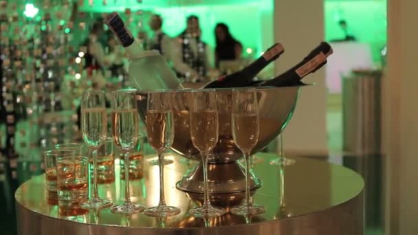 Бокалы шампанского и вина на столе, бутылка шампанского или вина в ведре на фоне танцующих людей, размытые силуэты людей — стоковое видео