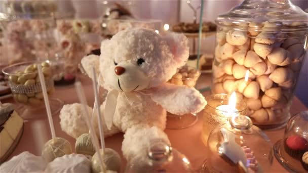 Candy bar in het restaurant, childrens party, verjaardag, een witte teddy beer met een vlinder op haar nek, stak een kaars, teddy bear op een tafel Candy bar, close-up — Stockvideo
