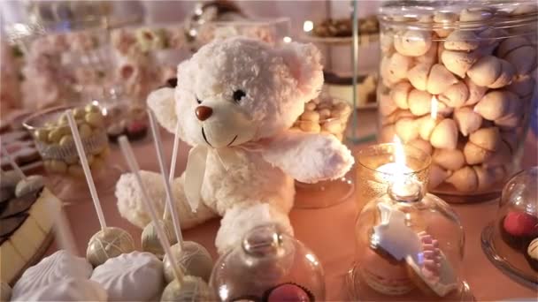 Candy bar al ristorante, festa per bambini, compleanno, un orsacchiotto bianco con una farfalla sul collo, candela accesa, orsacchiotto su un tavolo Candy bar, primo piano — Video Stock
