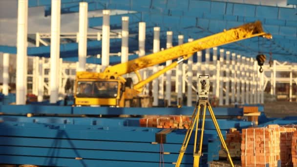 Optiska teodolit, byggare teodolit, konstruktion teodolit på bakgrunden av byggandet av en stor industribyggnad eller lagerställe, byggnadsarbeten — Stockvideo