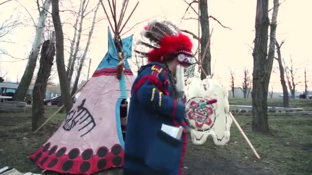 Североамериканский индеец в полном платье, мужчина в костюме, индийский танец с бубном на улице перед вигвамом — стоковое видео