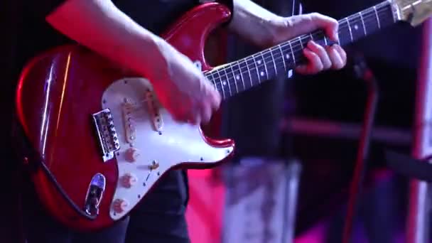 Muzikant speelt de gitaar, de hand en vingers van de gitarist, gitarist met de gitaar op de achtergrond van het drumstel, het concert op het podium, de muzikale groep — Stockvideo