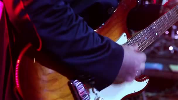 Muzikant speelt de gitaar, de hand en vingers van de gitarist, gitarist met de gitaar op de achtergrond van het drumstel, het concert op het podium, de muzikale groep — Stockvideo