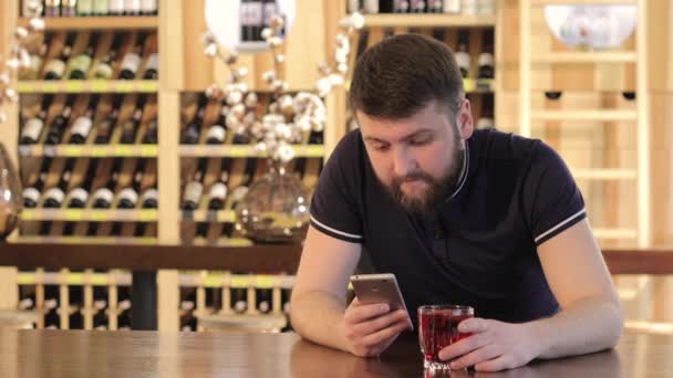 Hombre ipster bebiendo una bebida roja en un restaurante o cafetería, un joven usando un teléfono inteligente mientras bebe un cóctel rojo — Vídeo de stock