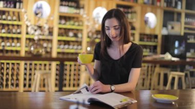 Genç bir kız kahve içer ve bir kafede bir moda dergisi okur veya Restoran, kadın okuma dergi ve içme kahve, şarap raf, arka plan üzerinde Restoran şarap