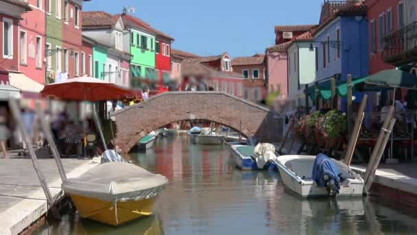 Burano adasındaki küçük bir kanal üzerinde köprü. Burano adası, insanlar adanın sokaklarında yürüyor. — Stok video