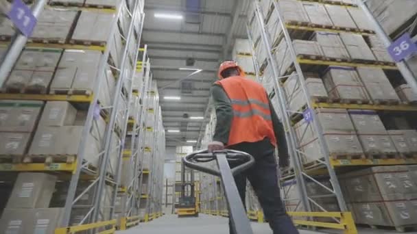 Un hombre con un chaleco naranja lleva una camioneta en un almacén — Vídeos de Stock