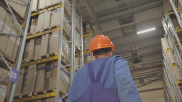 Un operaio passa per il magazzino, un operaio in uniforme alla fabbrica. Uomo in casco in fabbrica — Video Stock