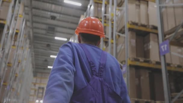 Ein Arbeiter geht durch das Lager, ein Arbeiter in Uniform in der Fabrik. Mann mit Helm in der Fabrik — Stockvideo