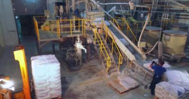 Torbaları taşıma bandına yüklüyorum. Vakum manipülatörü taşıma hattında torba kaldırıyor. Bir adam vakum manipülatörü kullanarak çantaları hareket ettiriyor..