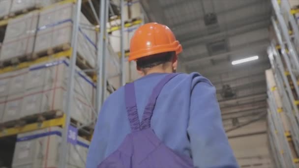 Pracownik przechodzi przez magazyn, pracownik w mundurze w fabryce. Mężczyzna w kasku w fabryce. — Wideo stockowe