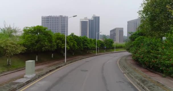 Vliegen langs de lege weg en opstijgen boven de bomen, met uitzicht op de Chinese stad — Stockvideo