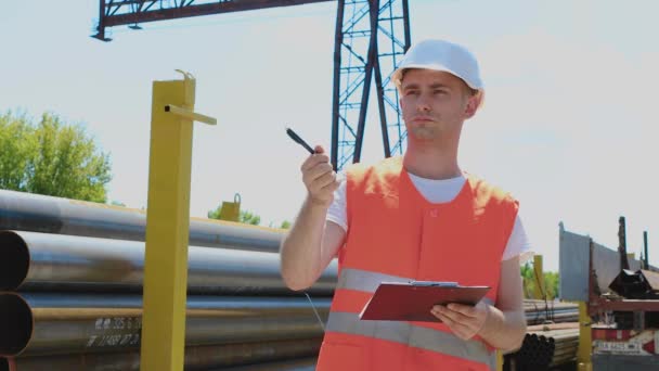 Un hombre en un almacén escribe a un cuaderno. El hombre en una fábrica escribe información en un cuaderno — Vídeos de Stock