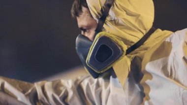 Koruyucu takım elbiseli bir adam büyük bir parça boya, bir sprey tabanca, büyük metal bir parça boyuyor.