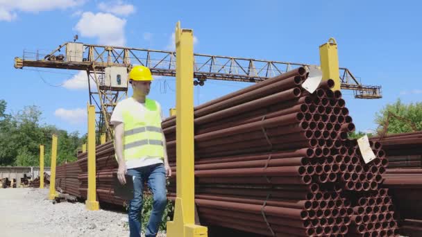 A raktár dolgozója fényes sárga mellényben és sisakban leltárt készít a fémről. A menedzser megszámolja a termékek számát — Stock videók