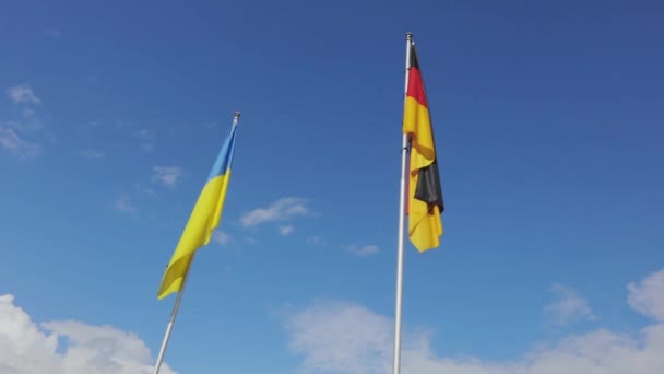 Oekraïense en Duitse vlag zwaaiend geïsoleerd met blauwe lucht op de achtergrond. Duitsland, Duitsland — Stockvideo