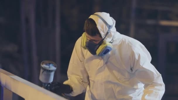 Een man in een beschermend pak schildert een groot deel, een spuitpistool, schildert een groot metalen deel — Stockvideo
