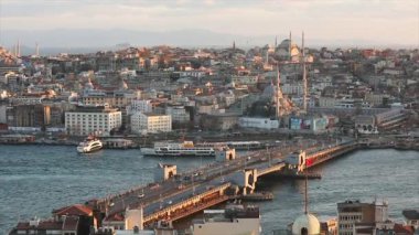 Gün batımında Galata Köprüsü ve camilerin manzarası. Bir sürü martı uçuyor, turist tekneleri yüzüyor.