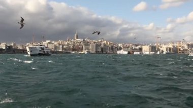 Galata Kulesi 'nin ön planda turistler ve martılarla dolu eğlence teknelerinin çekimi. Galata Kulesi 'nin arka planında tekneler, rüzgarlı hava
