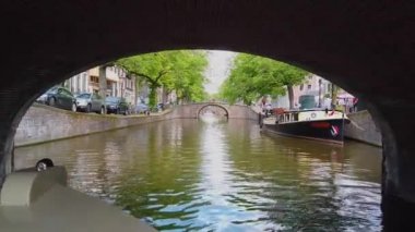Amsterdam 'da bir köprünün altından geçen turist teknesi. Nehrin üzerindeki köprü, Amsterdam. Amsetrdam 'da insanlar sokaklarda yürüyor