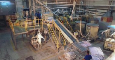 Torbaları taşıma bandına yüklüyorum. Vakum manipülatörü taşıma hattında torba kaldırıyor. Bir adam vakum manipülatörü kullanarak çantaları hareket ettiriyor..