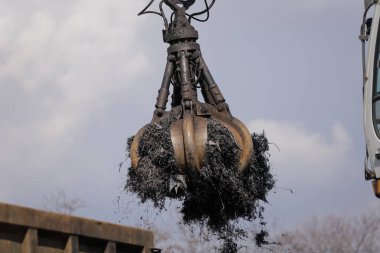Bir işçi hurdalıktaki arabalardan parçalanmış metalleri yüklemek için bir pençe kazıcı kullanıyor.