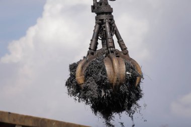 Bir işçi hurdalıktaki arabalardan parçalanmış metalleri yüklemek için bir pençe kazıcı kullanıyor.