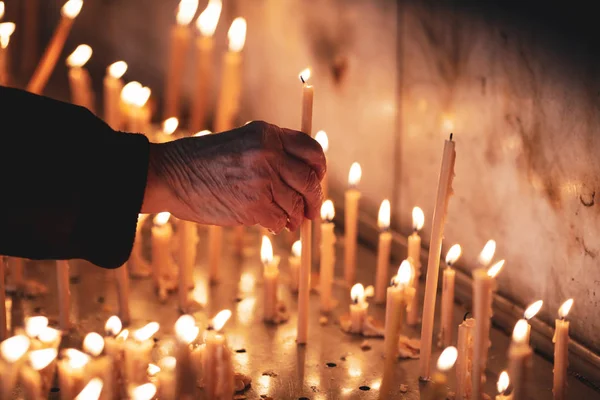 Dettagli con le mani di una vecchia che accende una candela all'interno — Foto Stock