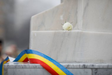 White rose on a white marble monument with the Romanian flag dur clipart