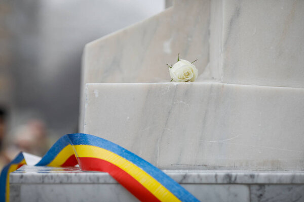 White rose on a white marble monument with the Romanian flag dur