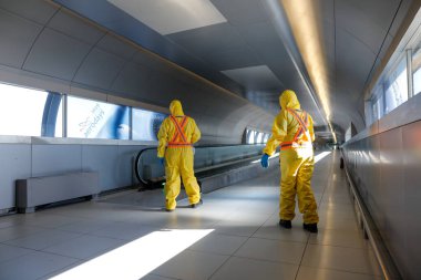 Otopeni, Romania - February 25, 2020: People wearing protective suits spray disinfectant chemicals on the Henri Coanda International Airport to prevent the spreading of the coronavirus. clipart
