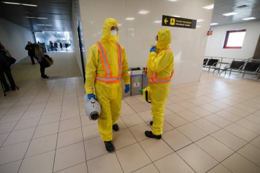 Otopeni, Romania - February 25, 2020: People wearing protective suits spray disinfectant chemicals on the Henri Coanda International Airport to prevent the spreading of the coronavirus.