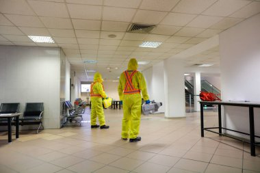 Otopeni, Romania - February 25, 2020: People wearing protective suits spray disinfectant chemicals on the Henri Coanda International Airport to prevent the spreading of the coronavirus.