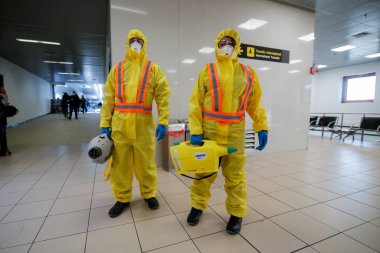 Otopeni, Romania - February 25, 2020: People wearing protective suits spray disinfectant chemicals on the Henri Coanda International Airport to prevent the spreading of the coronavirus.