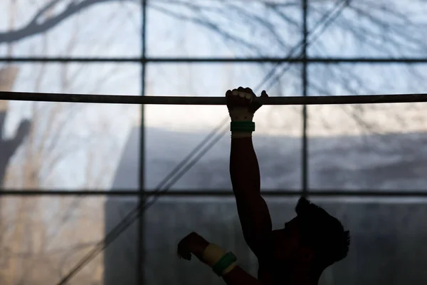 Silhouette of a young male gymnast training at the Horizontal Bar in a gym.