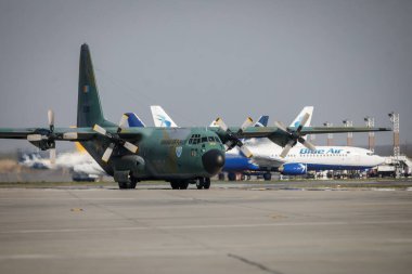 Otopeni, Romanya - 9 Nisan 2020: Lockheed C-130 Herkül askeri kargo uçağı Henri Coanda Uluslararası Havaalanı 'nda ticari uçaklar arasında.