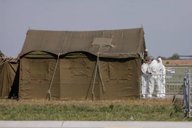 Otopeni, Romanya - 25 Nisan 2020: Bir askeri havaalanındaki askeri çadırın yakınındaki Covid-19 için koruyucu elbiseler giyen insanlar.