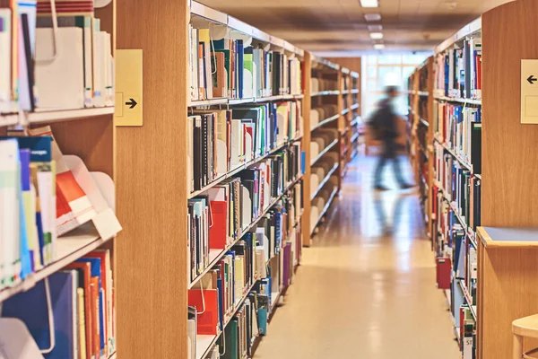 Студент проходит через проход между книжными шкафами в библиотеке — стоковое фото