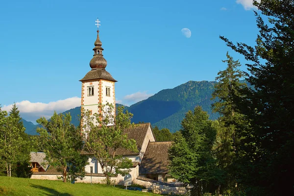 Eglise à Ribcev Laz, Slovénie situé sur la rive du lac Bohinj avec une lune de jour dessus — Photo