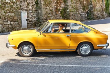 Genç adam sarı vintage Fiat 850 Spor Coupe 1970 circa İtalya'da serbest sürüş.