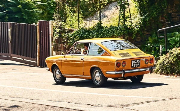 Young man driving yellow vintage Fiat 850 Sport Coupe released circa 1970 in Italy. — Stock Photo, Image
