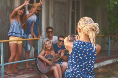Genç sarışın kız dreads ile ahşap tatil kabin yakınındaki onun smartphone ile onun Arkadaş grupları ait fotoğraf alır
